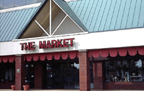 Exterior of a building with a sign that reads "THE MARKET" and a red awning, featuring large windows.