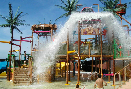 A colorful water play structure with slides and palm trees, featuring kids enjoying splashes and water features.