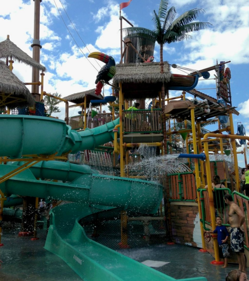 A colorful water park with slides, a play structure, and people enjoying the attractions under a blue sky.