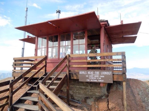 A red fire lookout cabin on a rocky outcrop, with wooden stairs and a sign reading "Devils Head Fire Lookout."
