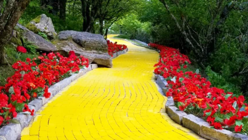 A winding yellow brick path surrounded by vibrant red flowers and lush greenery.