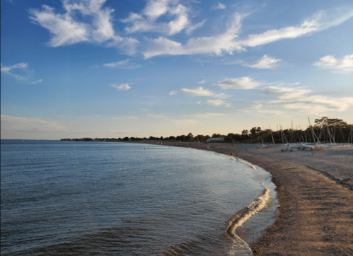 A serene beach scene at sunset, with gentle waves lapping at the shore and a clear sky dotted with clouds.