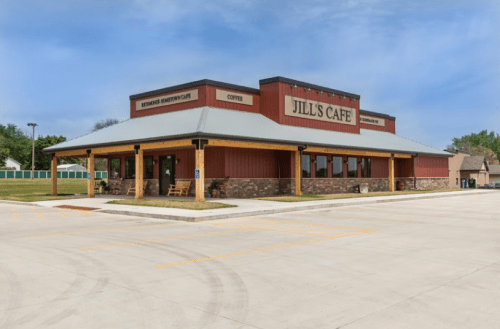 A modern café building with a red and brown exterior, featuring a sign that reads "Jill's Cafe" and a spacious parking area.