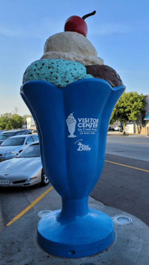 A large ice cream cone sculpture with three scoops and a cherry, marking the Visitor Center in a sunny area.