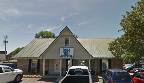 A two-story building with a metal roof, featuring a sign that reads "Sutter Health" and parked cars in front.
