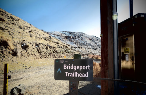 Sign for Bridgeport Trailhead with a hilly, snow-dusted landscape in the background. Clear blue sky above.