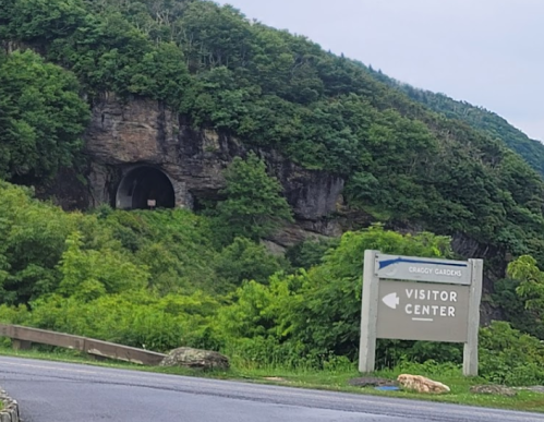 Sign for a visitor center at Craggy Gardens, with a tunnel entrance and lush greenery in the background.