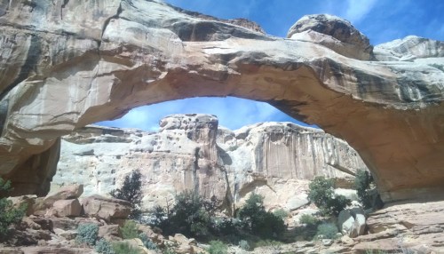 A natural stone arch stands tall against a blue sky, surrounded by rocky cliffs and sparse vegetation.