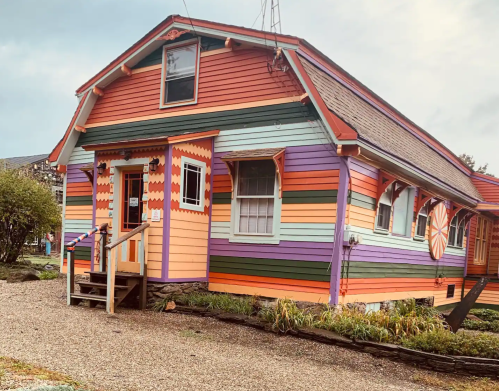 A colorful, striped house with a whimsical design, featuring orange, pink, and purple hues and a decorative entrance.