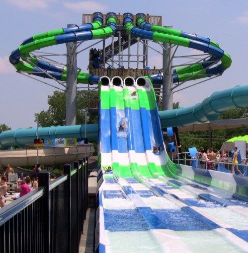 A water slide with multiple lanes, featuring riders splashing down, surrounded by a vibrant water park setting.