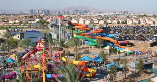 A vibrant water park with colorful slides, surrounded by homes and a city skyline in the background.