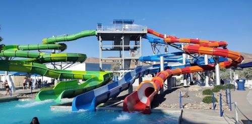 Colorful water slides twist and turn above a pool, with people enjoying the water park on a sunny day.