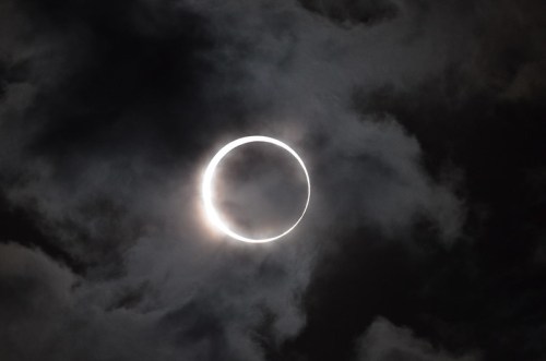 A dramatic view of an annular solar eclipse surrounded by dark, cloudy skies.