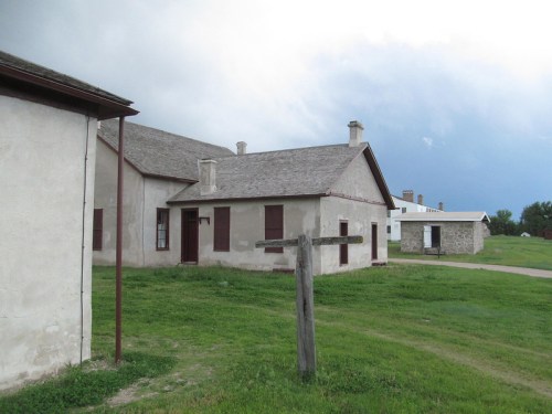 Historic building with a gray roof, wooden posts, and green grass, set against a cloudy sky.