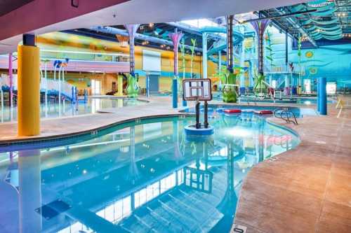 Indoor water park featuring a pool, slides, and colorful decor with palm trees and a basketball hoop.