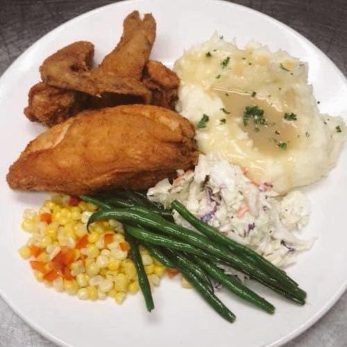A plate of fried chicken, mashed potatoes with gravy, coleslaw, green beans, and mixed corn.