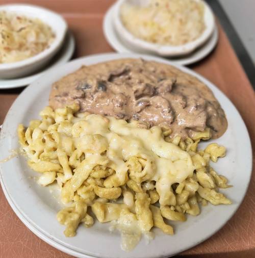 A plate of creamy pasta with cheese and beef stew, accompanied by two small bowls of coleslaw and rice.
