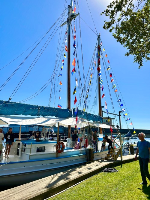 A sailboat docked with colorful flags, people boarding, and a clear blue sky in the background.