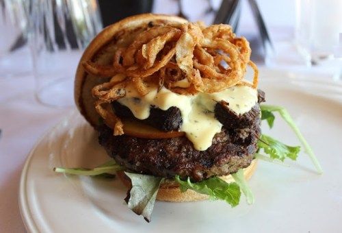 A gourmet burger with a beef patty, melted cheese, pickles, crispy onions, and lettuce on a toasted bun.