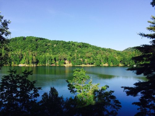 A serene lake surrounded by lush green hills under a clear blue sky.