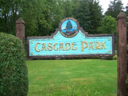 Sign for Cascade Park, featuring a blue background with gold lettering, surrounded by greenery.