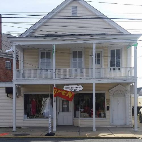 A two-story building with a porch, featuring a sign that says "OPEN" in the window of a shop.