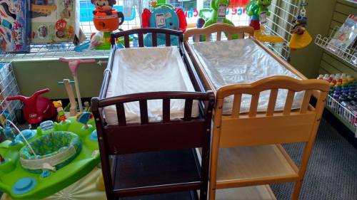 Two wooden baby cribs in a colorful store filled with toys and children's items.