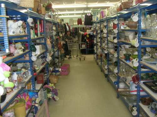 Aisle in a thrift store filled with shelves of various household items, including dishes, decorations, and clothing.