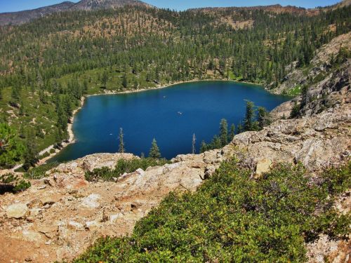 A serene blue lake surrounded by green trees and rocky terrain, set against a mountainous backdrop.