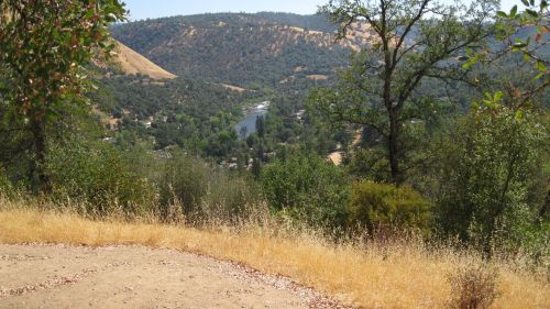 A scenic view of a river winding through green hills, surrounded by trees and dry grass under a clear blue sky.