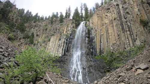 A tall waterfall cascading down a rocky cliff, surrounded by trees and greenery.