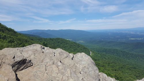 A panoramic view of lush green mountains and valleys under a blue sky with scattered clouds.