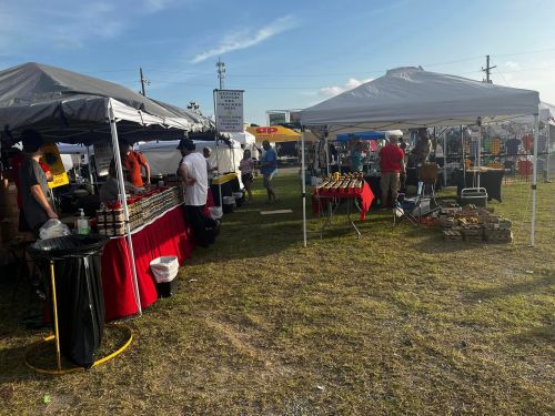 A bustling outdoor market with various vendor tents, people browsing, and products displayed on tables.