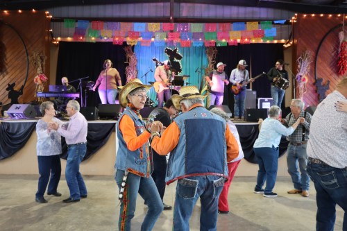 A lively dance scene with couples enjoying music on stage, decorated with colorful banners in a festive venue.