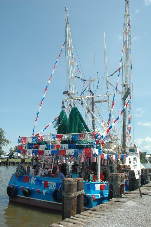 A decorated boat with colorful bunting is docked at a pier, with passengers onboard enjoying the view.