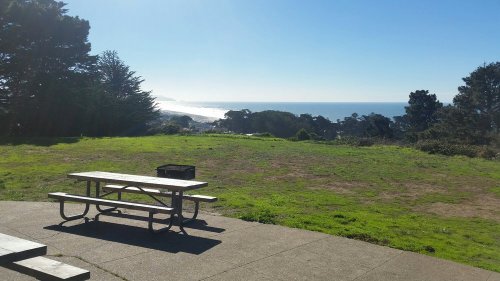 A picnic table on a grassy area overlooking a serene ocean view under a clear blue sky.