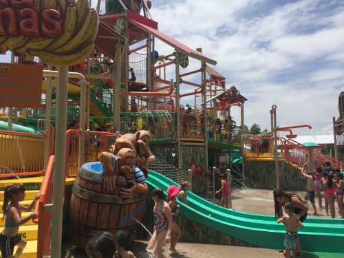 A vibrant water park scene with children playing, colorful slides, and water features under a sunny sky.