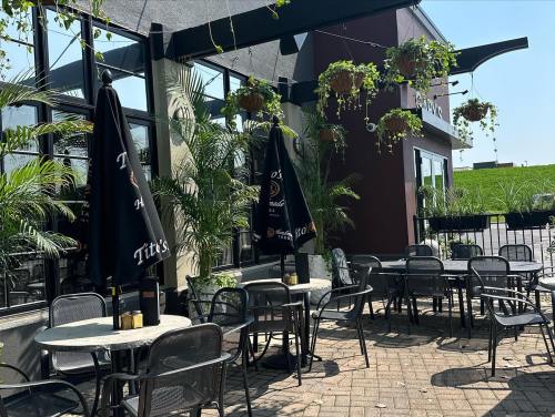 Outdoor dining area with tables, chairs, and large umbrellas, surrounded by plants and a sunny atmosphere.