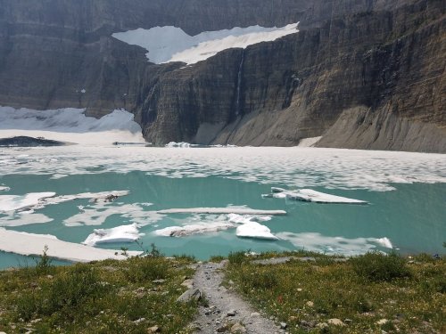 A serene glacial lake surrounded by rocky cliffs and icebergs, with a clear blue sky above.