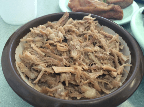 A bowl of shredded meat, likely pork, served as a dish, with a side of fried items in the background.