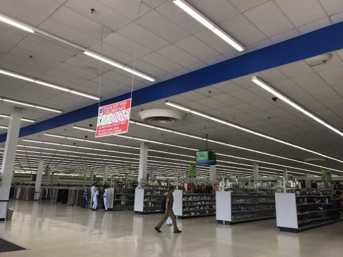 Interior of a retail store with clothing racks, bright lighting, and a large sign hanging from the ceiling.