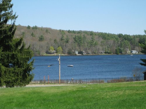 A serene lake surrounded by trees, with a boat on the water and a clear blue sky above.
