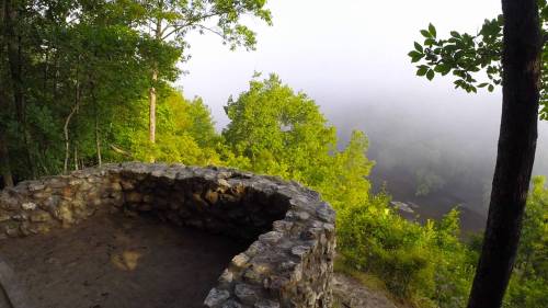 A stone overlook surrounded by lush green trees, with fog rolling over a valley below.