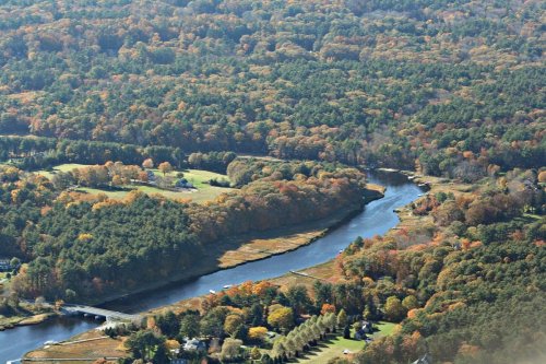 Aerial view of a winding river surrounded by vibrant autumn foliage and lush green fields.