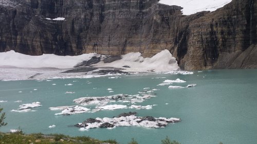 A serene glacial lake surrounded by rocky cliffs and icebergs, with snow-capped peaks in the background.