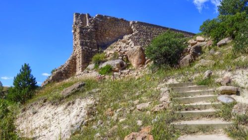 Ruins of a stone structure on a grassy hillside, with stone steps leading up to it under a clear blue sky.