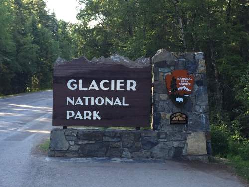 Sign for Glacier National Park, featuring stone and wood design, surrounded by trees and a clear sky.