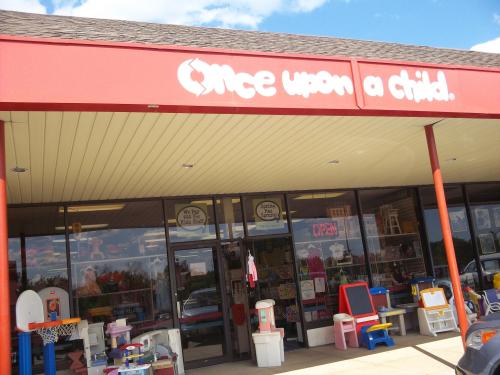 Exterior of a children's resale store, "Once Upon a Child," featuring colorful signage and various outdoor toys.