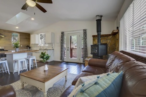 Cozy living area with a leather sofa, wooden coffee table, and a wood stove, featuring bright natural light and a modern kitchen.