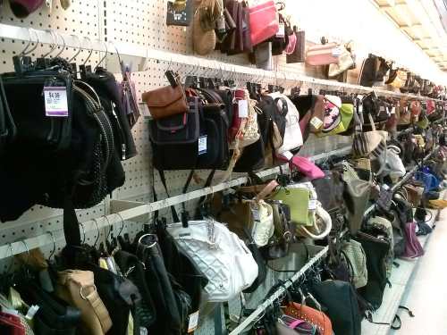 A display of various handbags and purses hanging on a pegboard wall in a retail store.